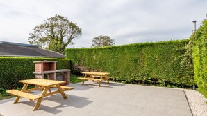 An outdoor patio area with two picnic tables and a brick barbecue grill.