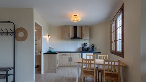 A modern kitchen with wooden cabinets, a dining table with chairs, a hanging light fixture, and a window with curtains.