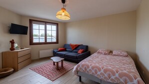 A bedroom with a bed, a sofa, a TV, a dresser, and a window.
