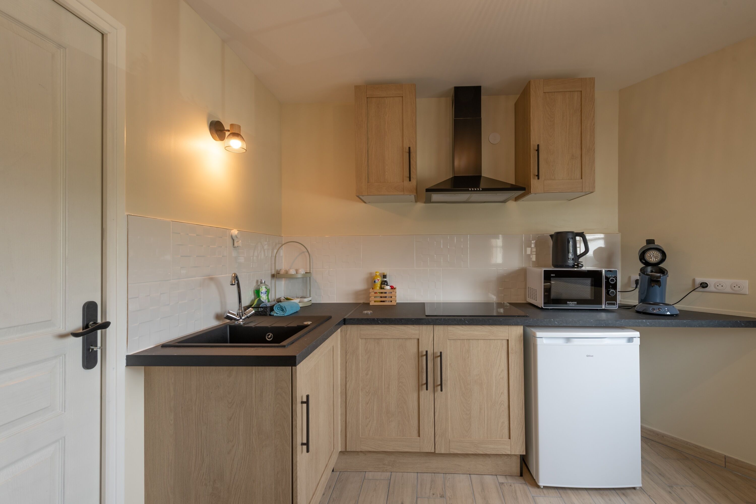 A compact kitchen with wooden cabinets, a built-in microwave, a coffee maker, and a dishwasher.