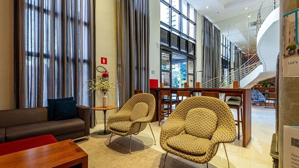 A modern lobby with a sofa, two patterned armchairs, a wooden coffee table, and a staircase leading to an upper level. - Modern, well located in Sampa next to the Faria Lima subway station (São Paulo)