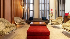A modern living room with a sofa, two armchairs, a red ottoman, and a wooden accent wall. - Modern, well located in Sampa next to the Faria Lima subway station (São Paulo)