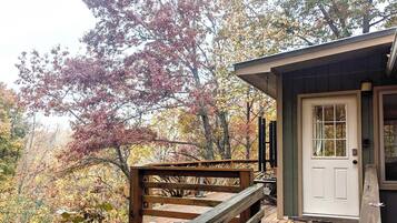A wooden deck with a white door, surrounded by autumn foliage.