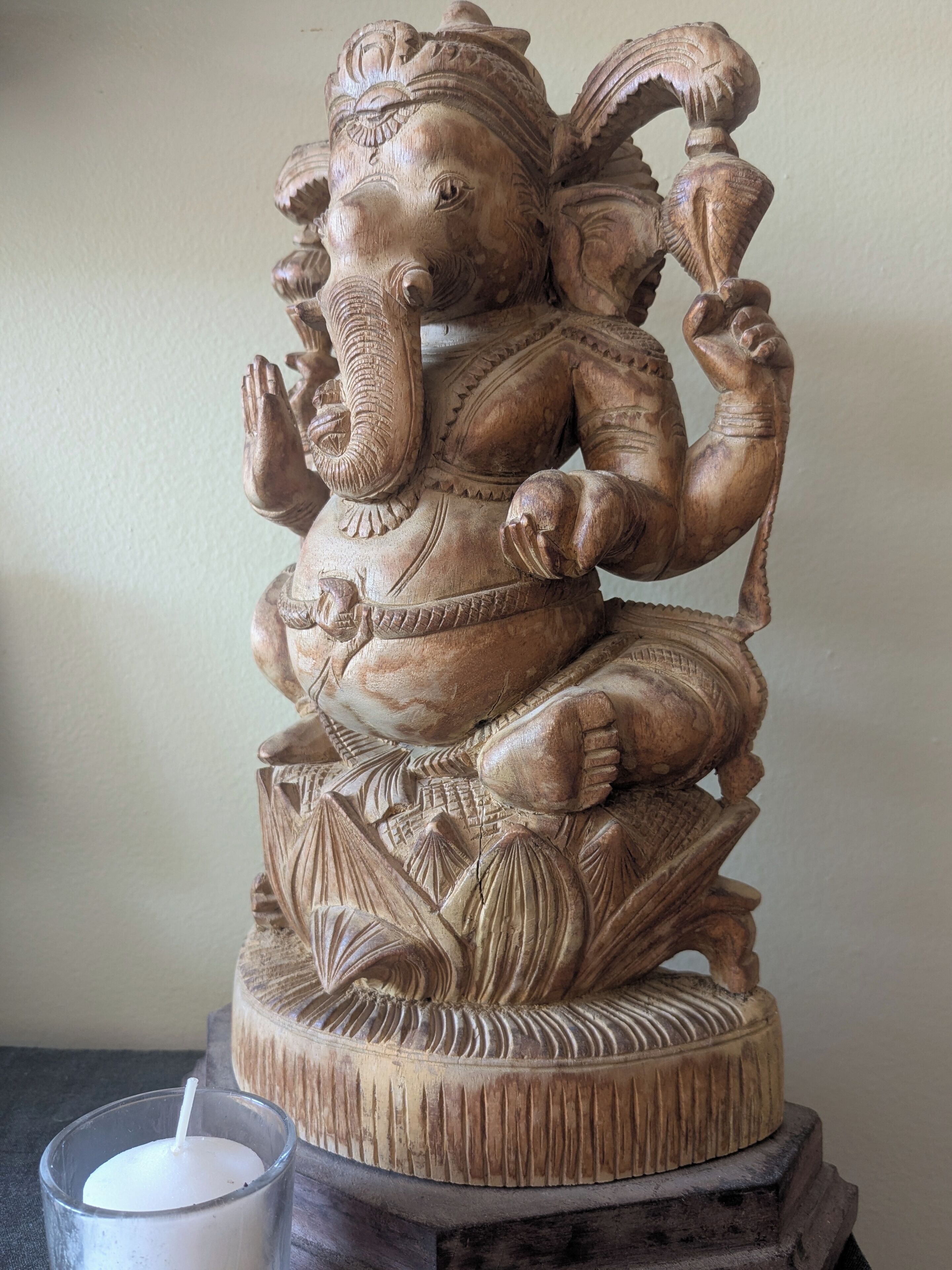 A wooden statue of a deity with intricate carvings, placed on a textured base.