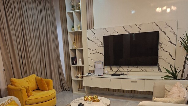 Een moderne woonkamer met een grote flatscreen-tv, witte banken en een salontafel.