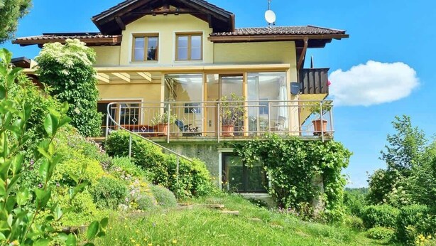 A two-story house with a balcony, surrounded by lush greenery. - Gipfelgold | Zugspitze View · Balcony · Königscard (Nesselwang)