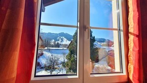 A window with a view of a snowy landscape and buildings. - Gipfelgold | Zugspitze View · Balcony · Königscard (Nesselwang)