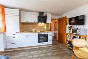 Eine kleine Küche mit weißen Schränken, einer Mikrowelle, einem Herd und einem Fernseher an der Wand.