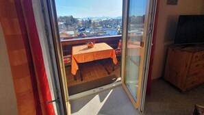 A balcony with a table and chairs, a television, and a view of a town. - Gipfelgold | Zugspitze View · Balcony · Königscard (Nesselwang)