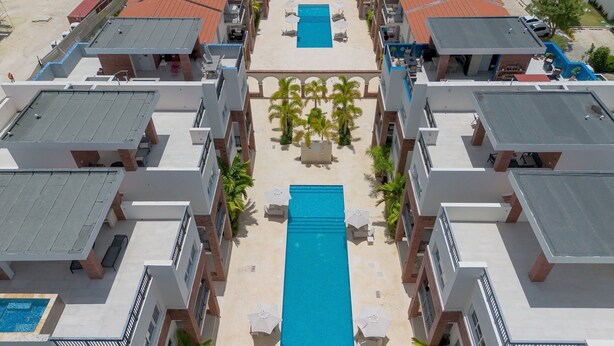 Een modern hotel met een centraal gelegen zwembad, meerdere balkons en een binnentuin met palmbomen.