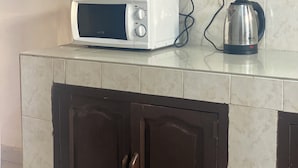 A kitchen with a microwave, kettle, and a shelf above the counter. - Osim homes (Arusha)