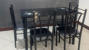 A dining area with a black table and chairs, a tiled floor, and a plain wall. - Osim homes (Arusha)