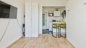 A compact kitchen with a microwave, kettle, and a small dining area with two green chairs.