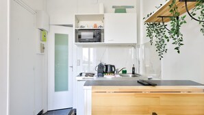 A compact kitchen with a microwave, stove, and sink. There is a small dining area with a wooden table and chairs.