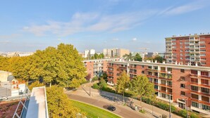 A multi-story residential building with balconies, a parking area, and a clear sky.
