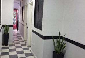 Un pasillo con piso a cuadros, plantas en macetas y una puerta con un ventanal negro texturizado.