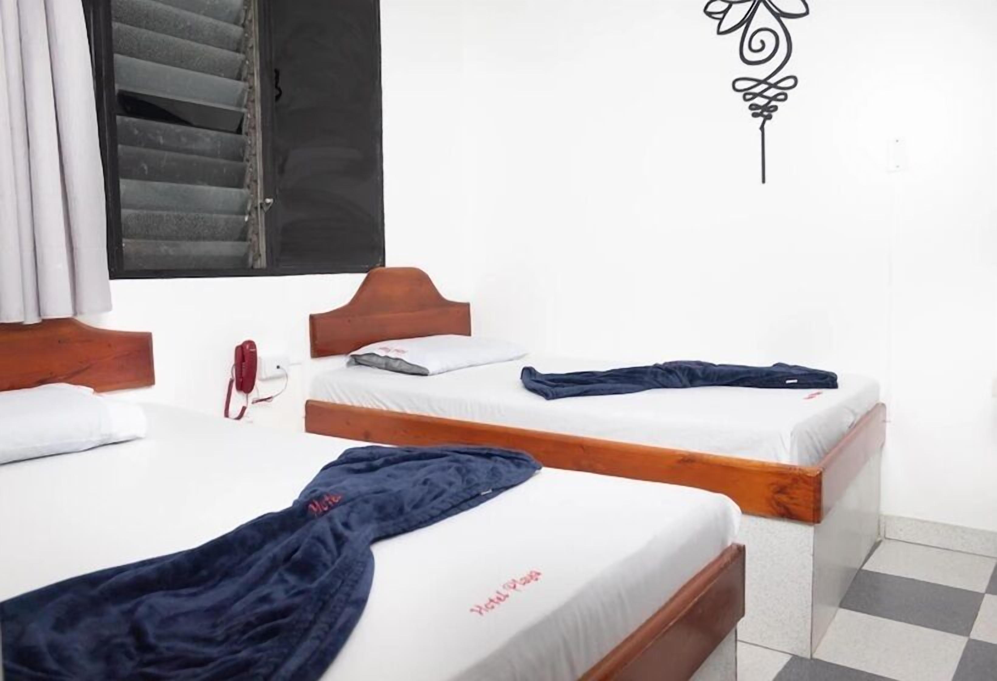 A hotel room with two single beds, a wooden headboard, a window with blinds, a wall decoration, and a checkered floor.