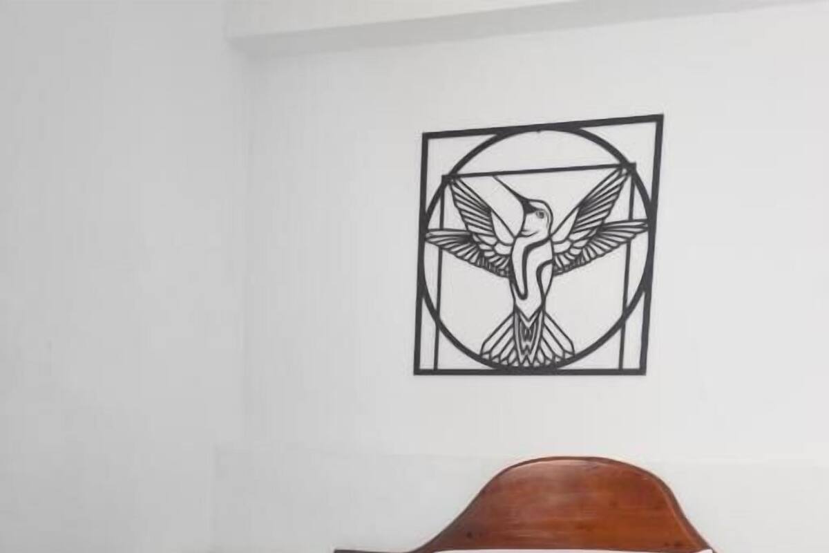 Ένα μονό κρεβάτι με ξύλινο προσκέφαλο, ένα λευκό μαξιλάρι και μια σκούρα μπλε κουβέρτα. Ένα μικρό λευκό κομοδίνο βρίσκεται στα αριστερά του κρεβατιού. Ένα ασπρόμαυρο έργο τέχνης με θέμα ένα πουλί είναι τοποθετημένο πάνω από το κρεβάτι.