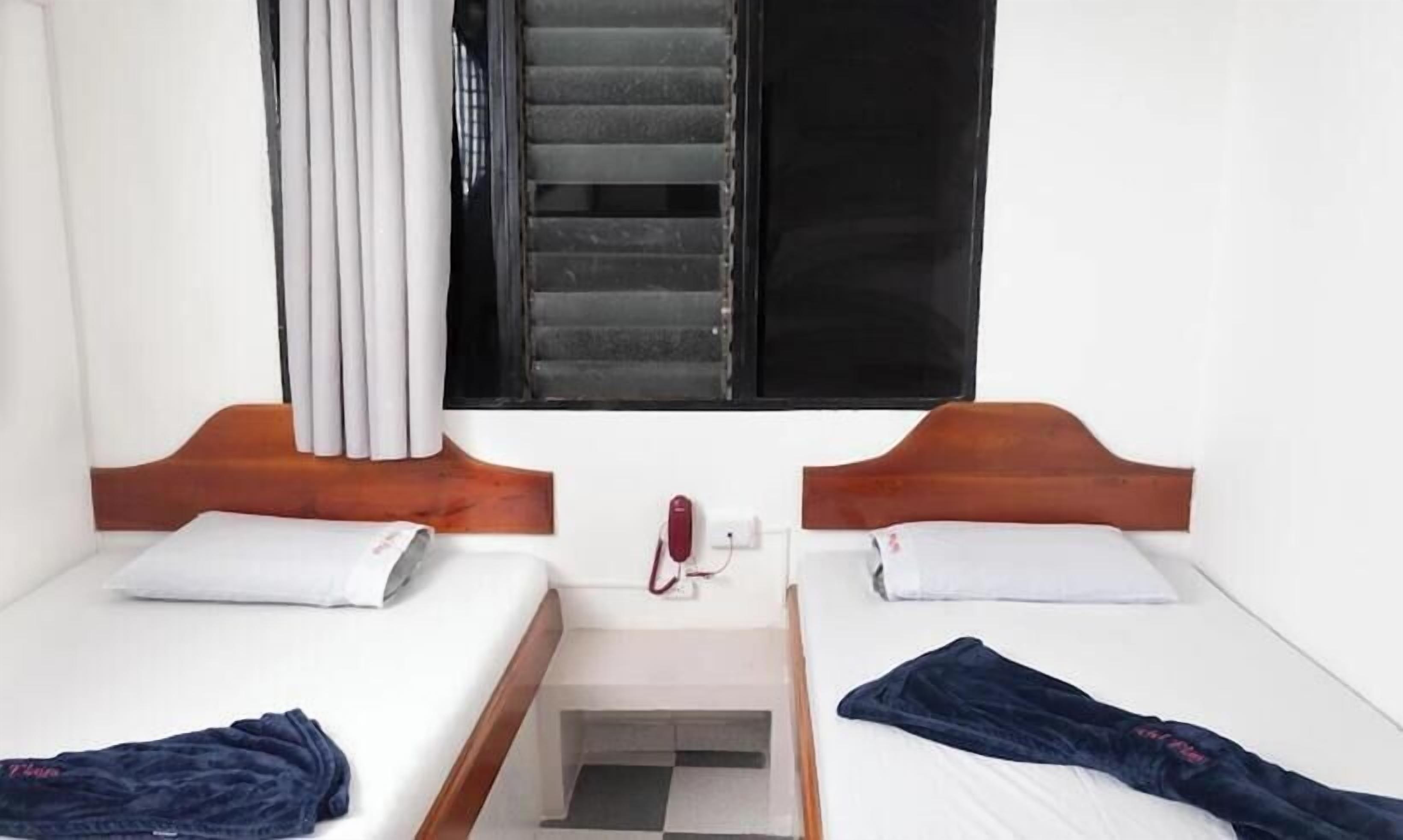 Una habitación de hotel con dos camas individuales, un ventanal con cortinas, un teléfono y un piso a cuadros.