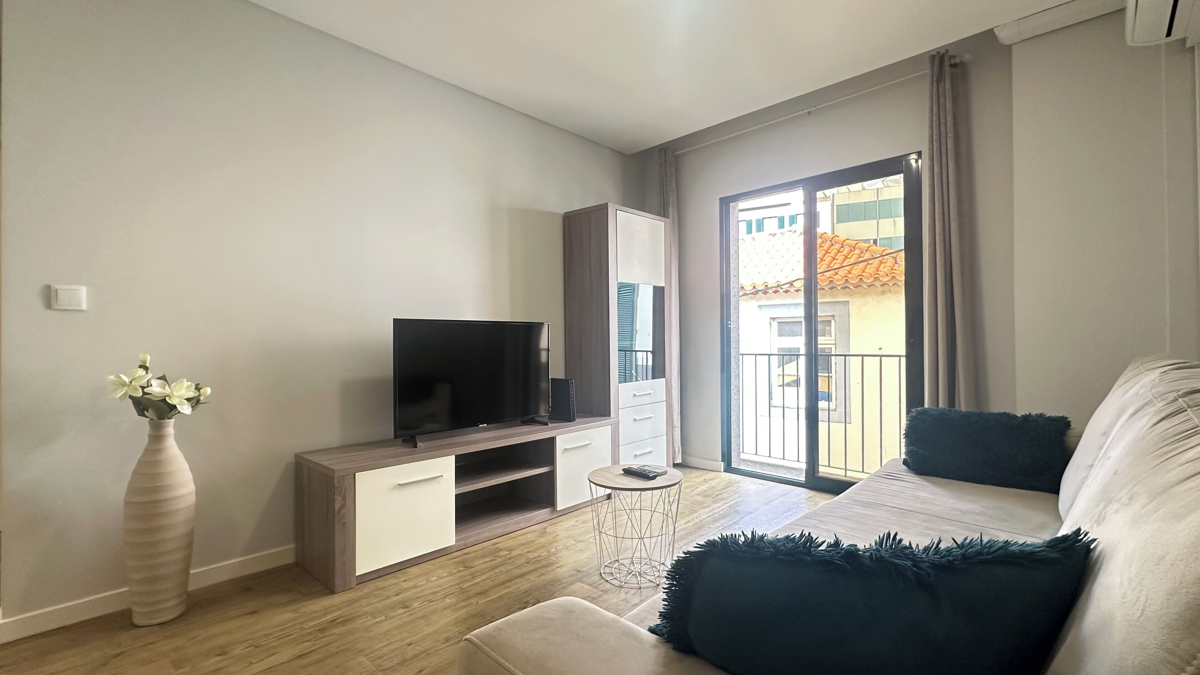 Una sala de estar moderna con un televisor de pantalla plana, un mueble blanco, una mesita redonda y un sofá con cojín oscuro.