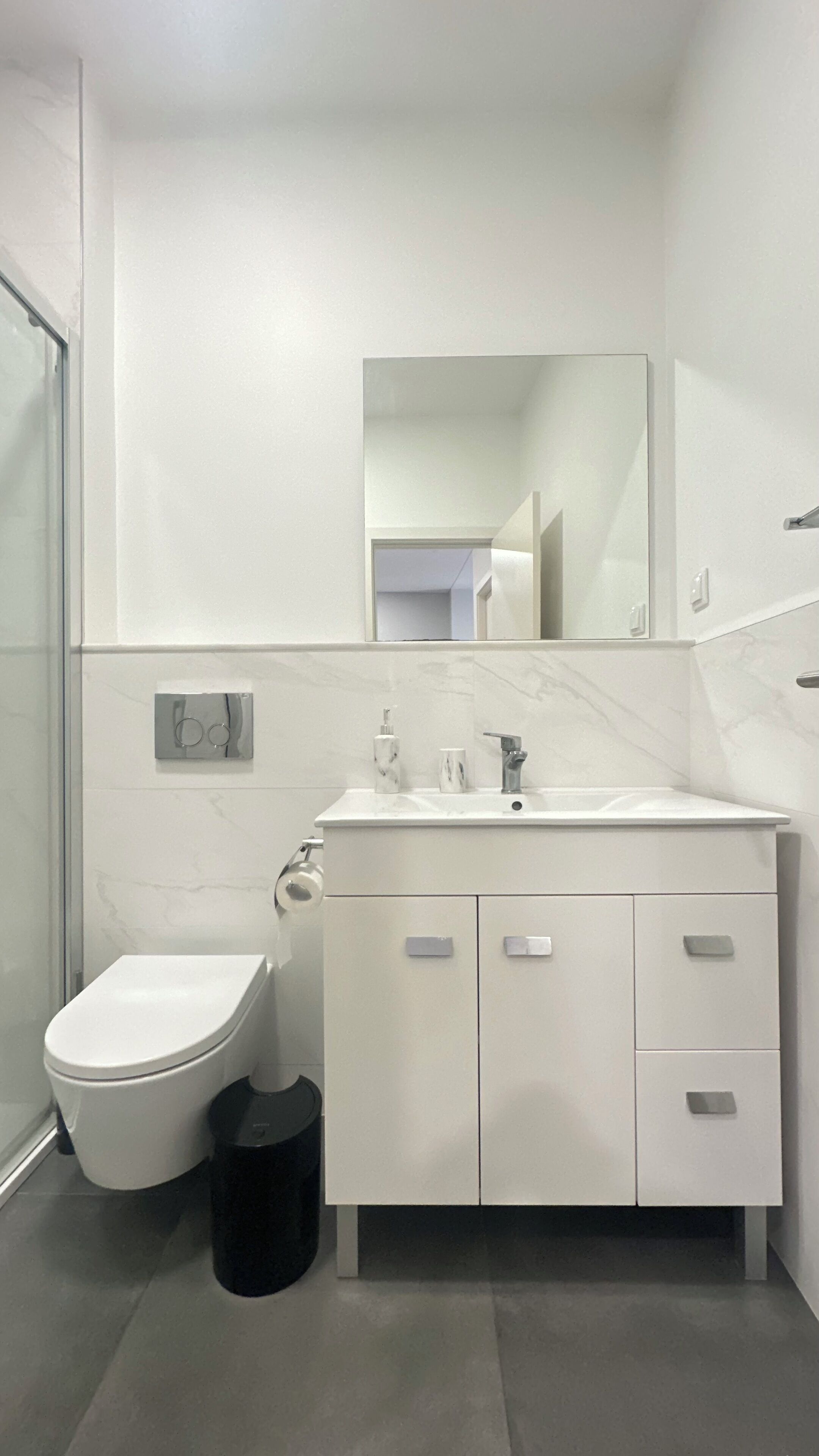 A modern bathroom with a white toilet, a sink with a marble countertop, and a mirror above the sink.