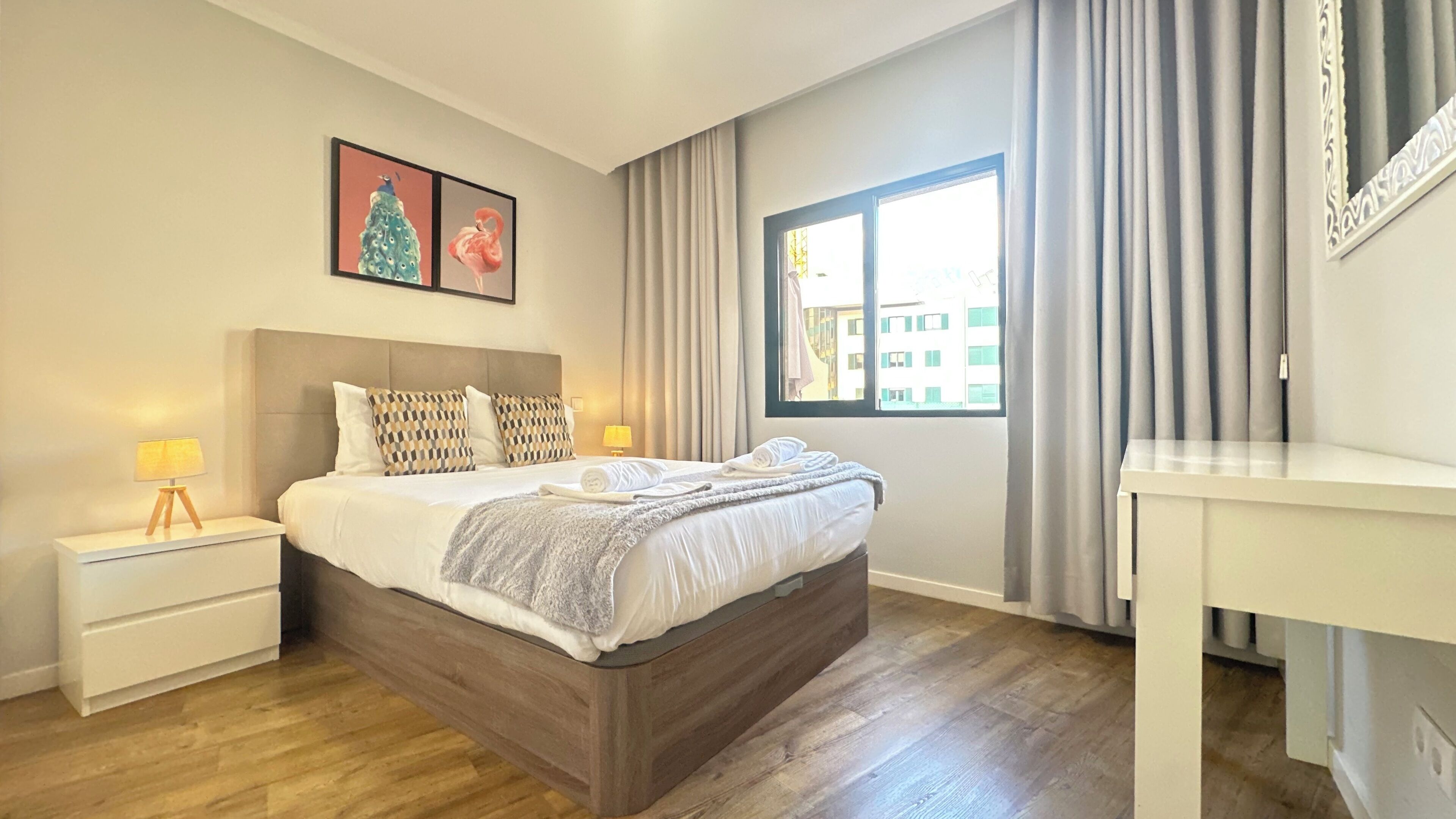 A hotel room with a bed, bedside tables, a desk, and a window with curtains.