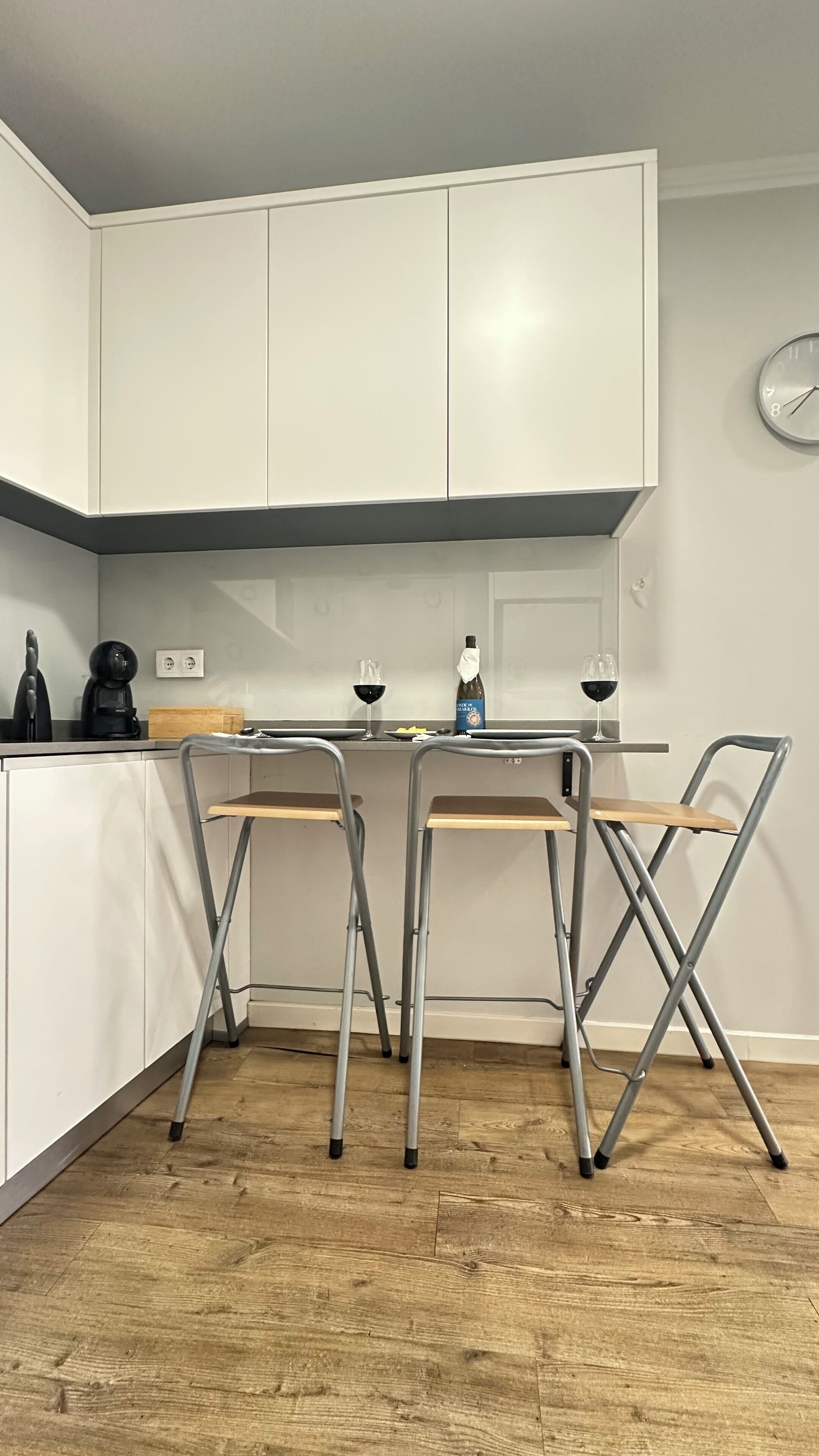 Une cuisine compacte avec des meubles blancs, un plan de travail en bois et une table pliante accompagnée de quatre chaises.