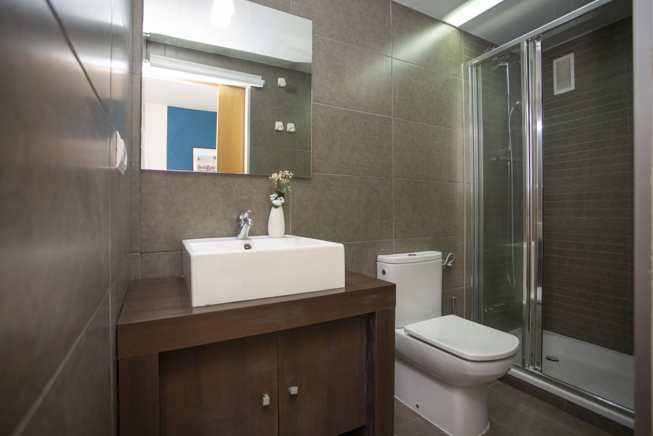 Et badeværelse med en hvid vask, toilet og en bruseniche med glasvægge.