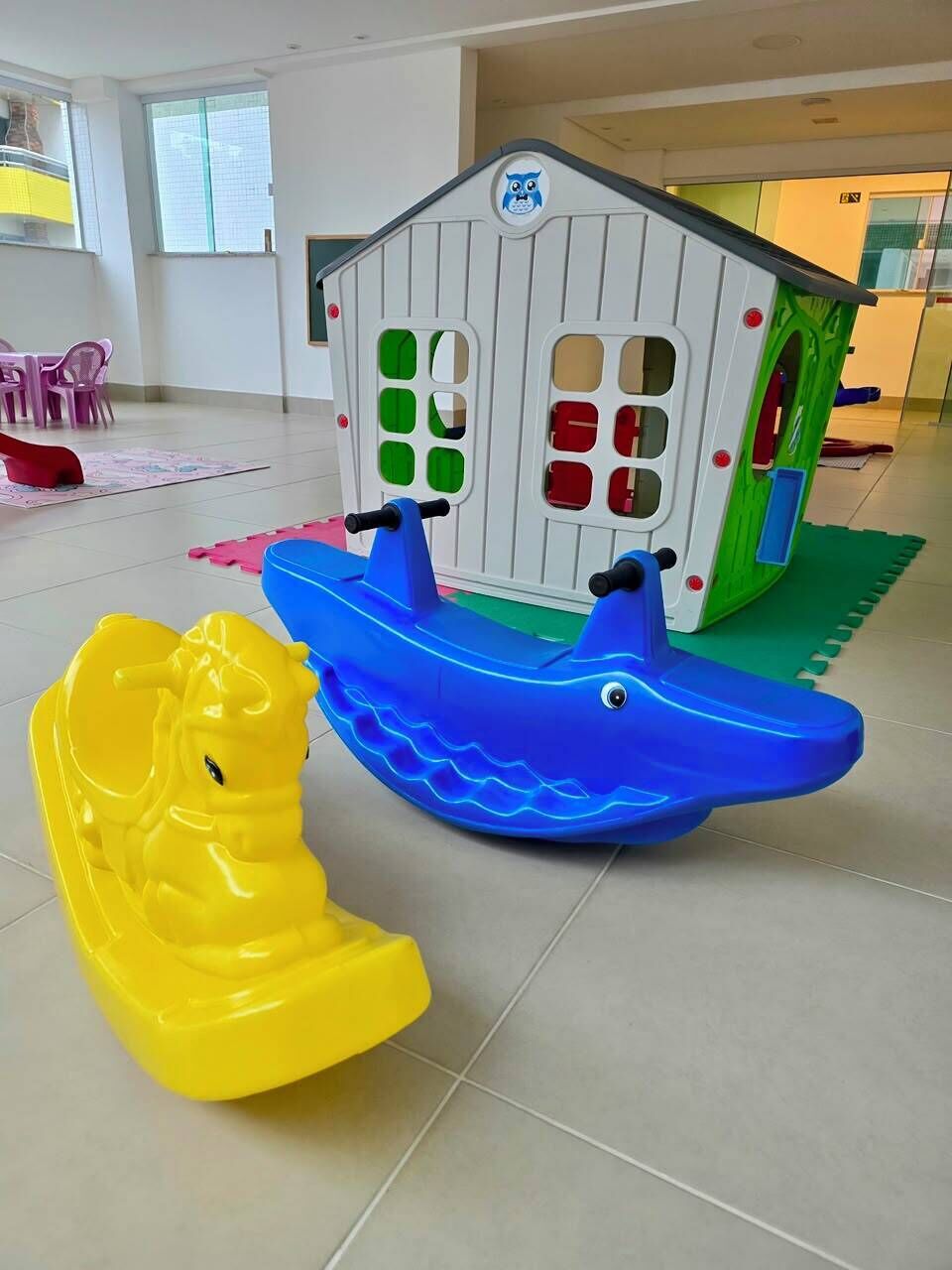Ein Spielbereich mit einem Haus, einem gelben Schaukelpferd und einem blauen Boot.