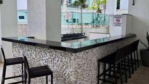A bar area with a stone counter, black chairs, and a view of a building with balconies.