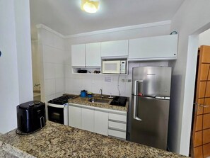 Una cocina compacta con armarios blancos, un refrigerador de acero inoxidable, un microondas, una estufa a gas y una cafetera.