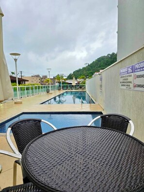 Un área de piscina en la azotea con una mesa y sillas, rodeada por una valla baja y un letrero que indica los servicios.