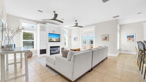 A spacious living area with a white sofa, a TV, ceiling fans, and a view of the outdoors. - ☀️Stunning Private Pool | Golf Cart | 30A | Topsail (Santa Rosa Beach)