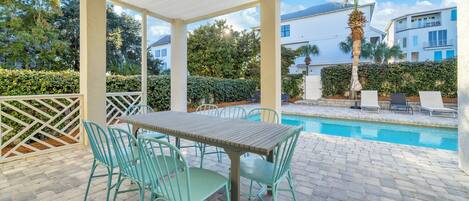 A covered patio with a pool, outdoor furniture, and a view of neighboring houses.