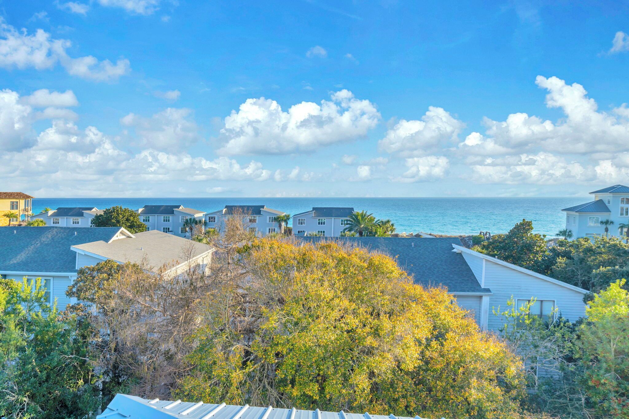 Zona residencial costeira com casas, céu claro e o oceano ao fundo.