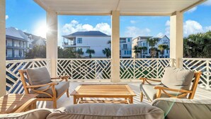 A covered outdoor seating area with wicker furniture and a wooden table, overlooking a residential neighborhood with houses and palm trees. - ☀️Stunning Private Pool | Golf Cart | 30A | Topsail (Santa Rosa Beach)