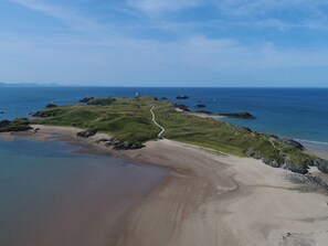 An aerial view of a coastal landscape with a winding path, grassy hills, and a lighthouse. - Rhows (Llanfairpwllgwyngyll)