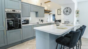 A modern kitchen with grey cabinets, a central island, bar stools, and a wall clock. - Rhows (Llanfairpwllgwyngyll)