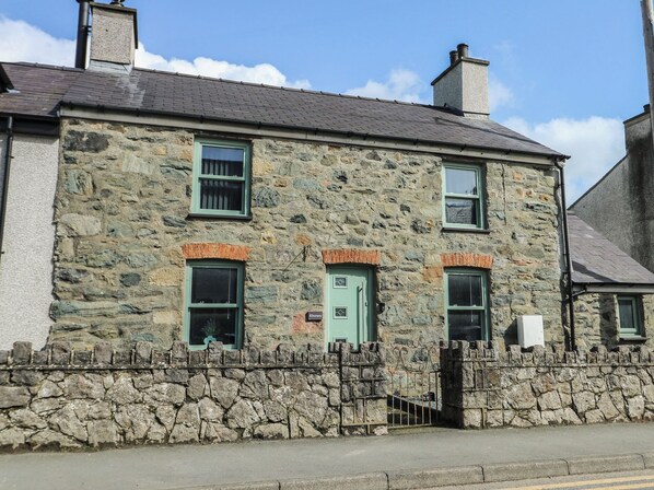 A stone building with a traditional design, featuring a stone wall, a metal gate, and a green door. - Rhows (Llanfairpwllgwyngyll)