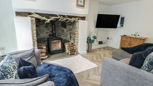 A cozy living room with a stone fireplace, a television mounted on the wall, and a wooden cabinet. - Rhows (Llanfairpwllgwyngyll)