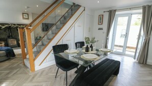 A modern dining area with a glass table, black chairs, and a wooden staircase. - Rhows (Llanfairpwllgwyngyll)