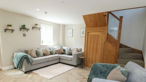 Ein modernes Wohnzimmer mit Fischgrätparkett, einem grauen Ecksofa, einem kleinen runden Tisch und einer Holztreppe.
