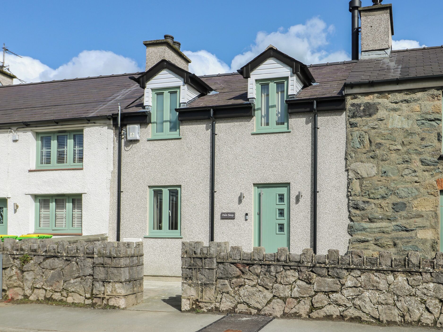 A two-story building with stone walls, green shutters, and a stone wall entrance.