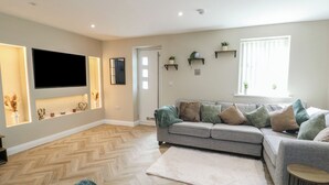 Ein Wohnzimmer mit grauem Sofa, Flachbildfernseher, Holzboden und einem weißen Teppich.