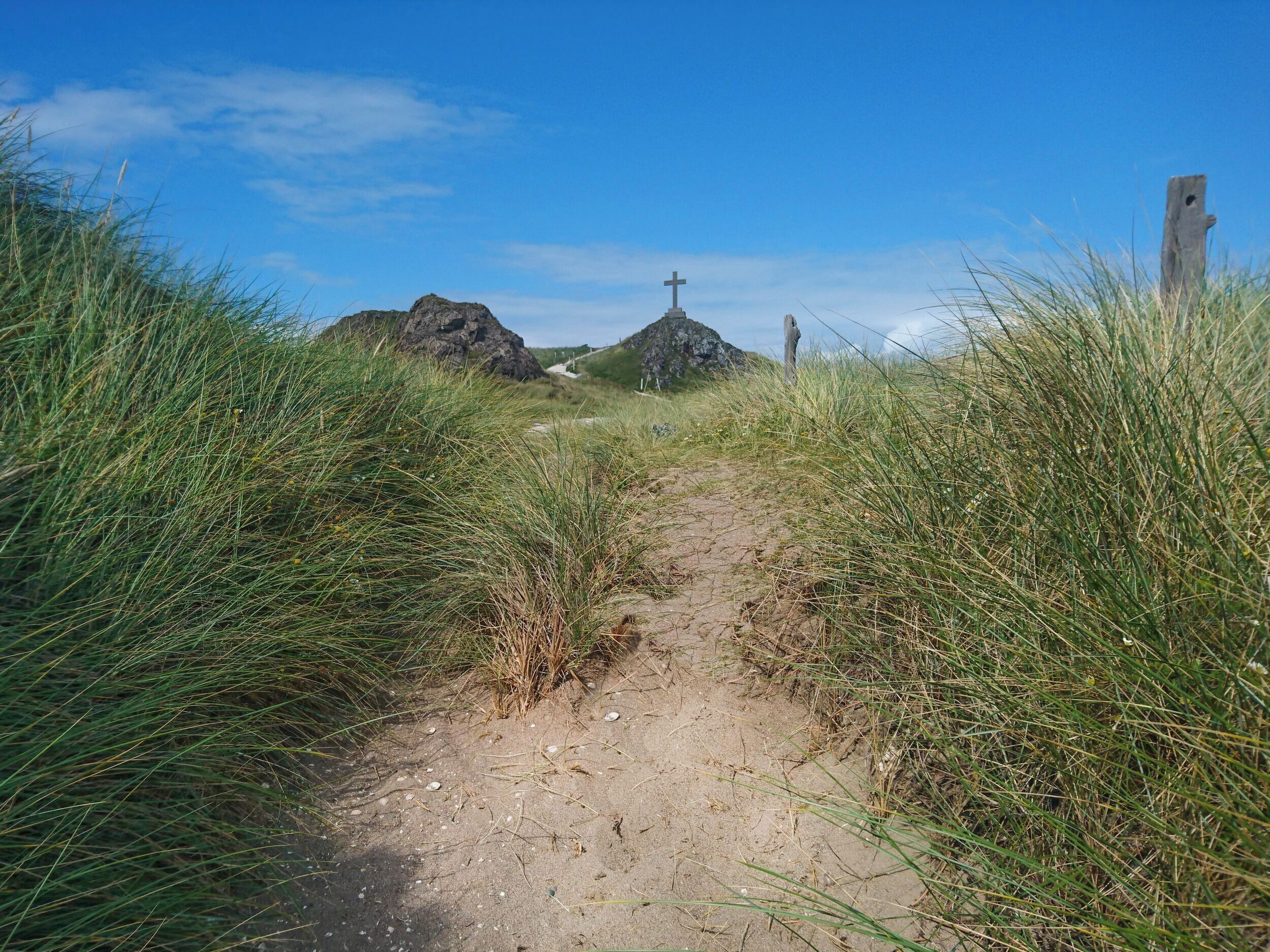 A dirt path leading to a rocky area with a cross monument.