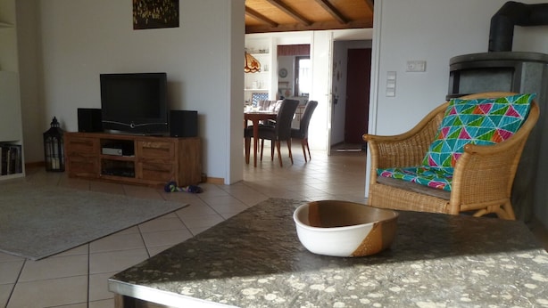 A living room with a television, a wicker chair, a dining area, and a kitchen with a stove. - Holiday Home "Unteres Hart" – Spacious and Comfortable (Gomadingen)