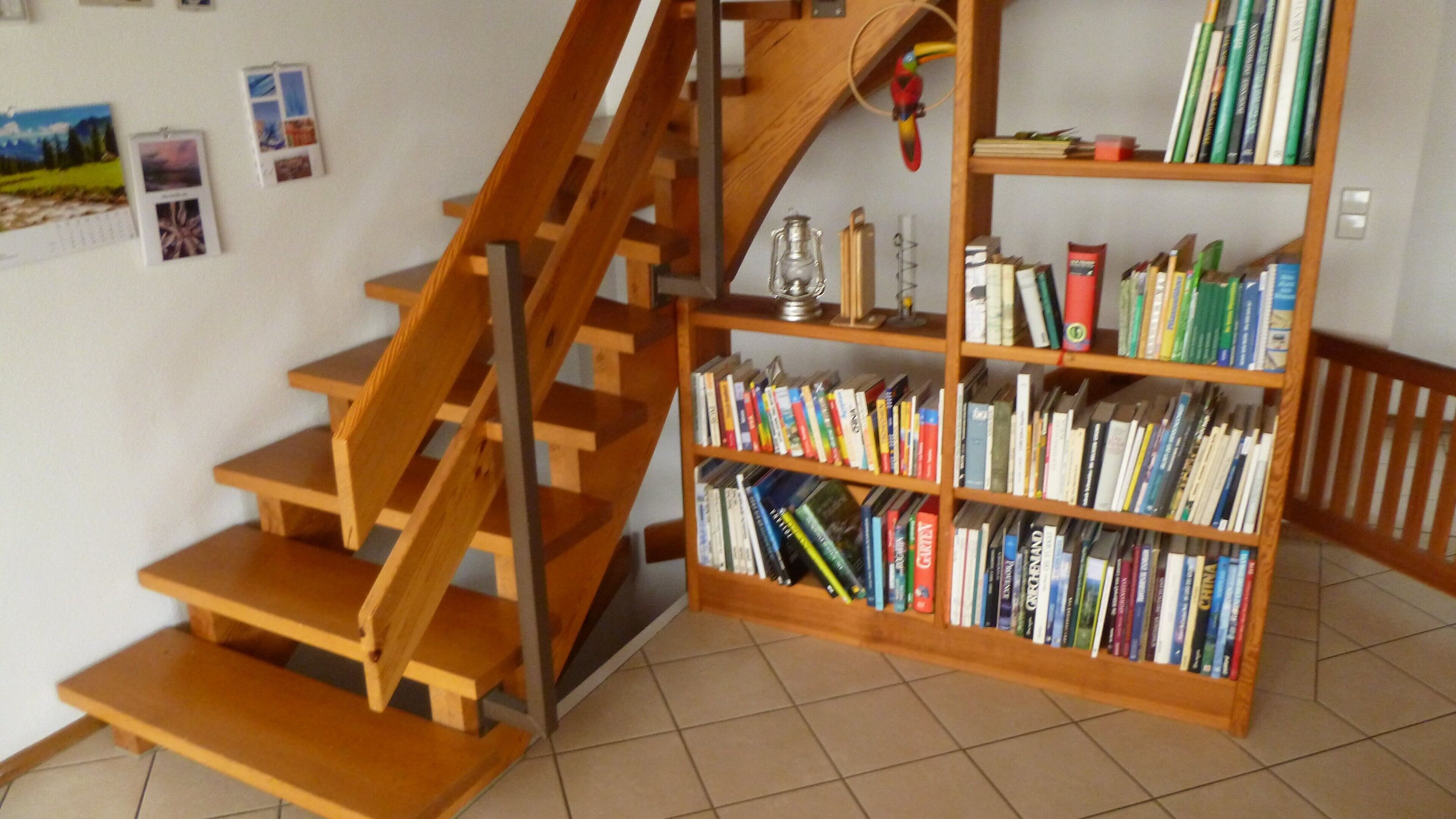 Eine Treppe mit Holzboden und Geländer, die zu einem Bücherregal mit Büchern führt.