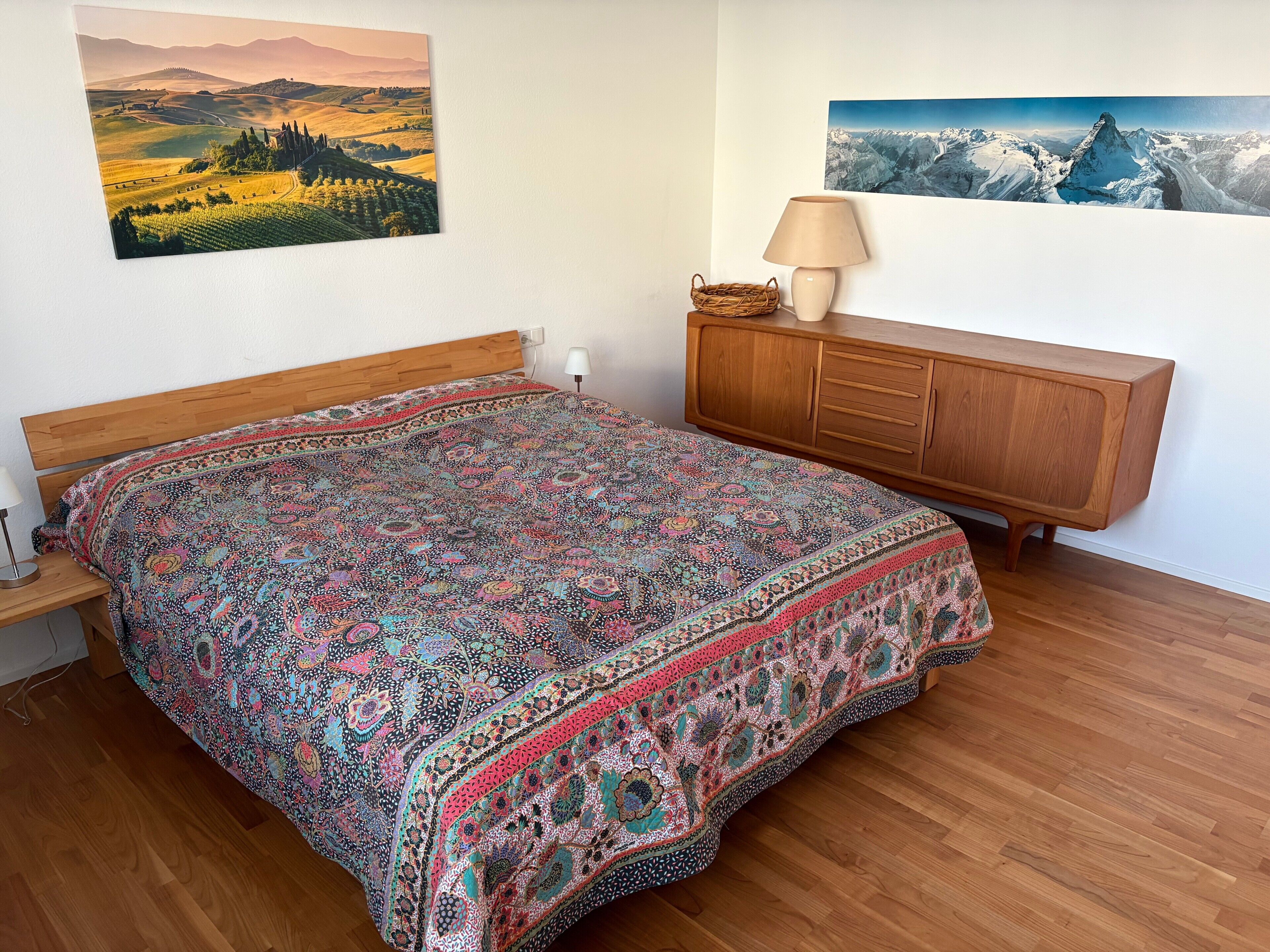 Ein Schlafzimmer mit einem hölzernen Bett, einer Holzkommode und zwei Landschaftsbildern an der Wand.