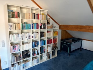 A room with a large bookshelf filled with books, a small table, and a sloped ceiling with wooden beams. - Holiday Home "Unteres Hart" – Spacious and Comfortable (Gomadingen)