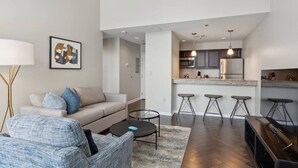 Un salon moderne avec un canapé, une table basse et un téléviseur. Il y a également un coin cuisine avec des tabourets de bar et un comptoir.